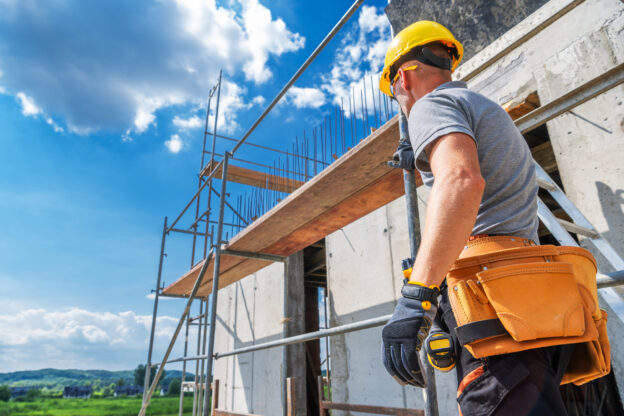 Trabalhador da construção civil utilizando a locação de andaimes em obra para aumentar a produtividade e segurança