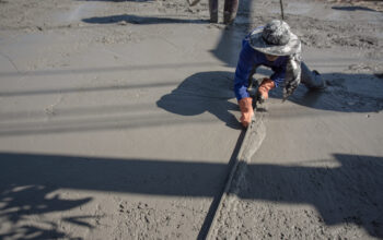 Trabalhador nivelando concreto em obra, etapa que pode ser facilitada pelo uso da fresadora de piso compacta.