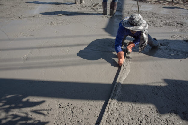 Trabalhador nivelando concreto em obra, etapa que pode ser facilitada pelo uso da fresadora de piso compacta.